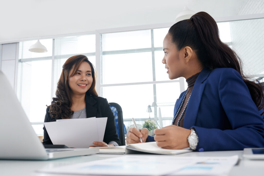 Smiling businesswoman discussing business ideas with colleague and taking notes in planner